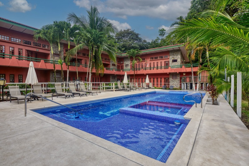 Pool and jacuzzi at Hotel Playa Bejuco framed by palms and the two-story red hotel building