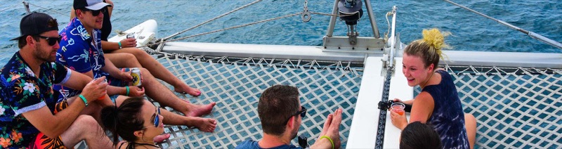Guests relaxing on the netting at the bow of a Lazy Lizard catamaran over blue water